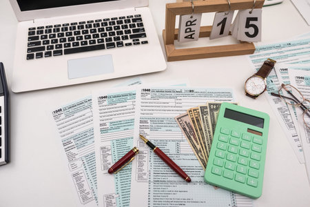 Blank personal income tax return with dollar bills and calculator and pen on calendar page marked...