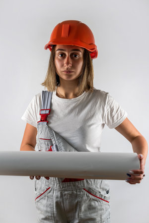 young woman in a construction worker's uniform and a helmet on her head posing for a portrait isolated on a white background. portrait of a woman. builder. architectの写真素材
