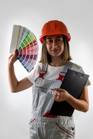 beautiful young girl builder stands in a hard hat and with color samples in hands for choosing the color of the wall. The profession of a woman builder. isolated on white backgroundの写真素材