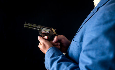 Sniper man in black suit gesturing and boldly holding gun on isolated black background. Concept for...