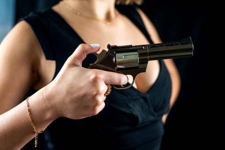 cropped photo of woman in sexy black dress with revolver in hand for shooting isolated on black...