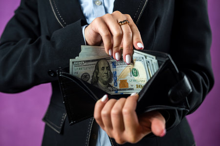 Close-up of a woman's hands putting a hundred dollar bill into her purse. Focus on the Purse. money. dollars in walletの写真素材