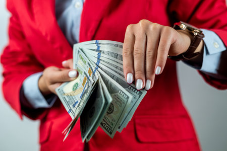 Portrait of beautiful hands of young woman in red clothes with dollars in them standing isolated on white background. showing money banknotes. woman boss business. money. cashの写真素材