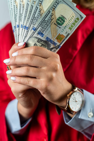 Portrait of beautiful hands of young woman in red clothes with dollars in them standing isolated on...