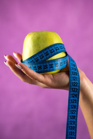 woman who wants to lose weight with an apple and a tape measure isolated on a white background. health conceptの写真素材