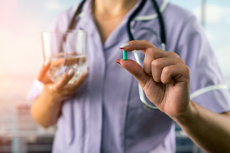cropped photo of female doctor holding pill and glass of water in two hands in hospital. doctor holds medicine for patient. people's healthの写真素材