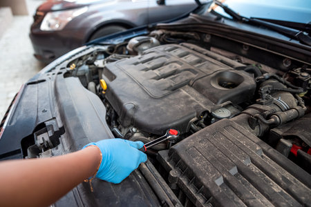 car mechanic repairs a car engine near a car with an open hood. car maintenance. repair services.の写真素材