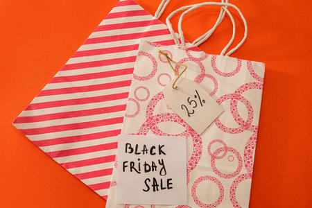 pink bags with the inscription black friday and a discount coupon on the side isolated on an orange...