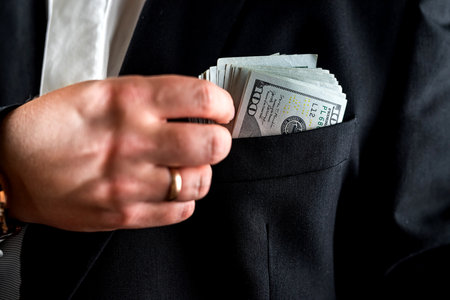 Close-up of a businessman or bank employee counting one hundred dollar bills in front of him with...