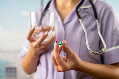cropped photo of female doctor holding pill and glass of water in two hands in hospital. doctor holds medicine for patient. people's healthの写真素材