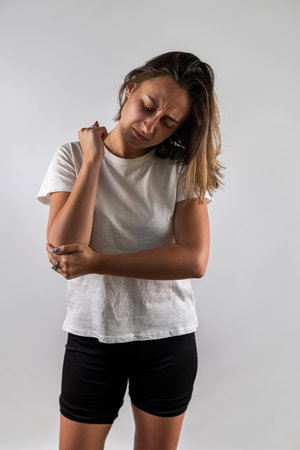 Brunette girl feels elbow pain wearing summer clothes isolated on white background. pain in hands joint painの写真素材