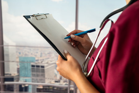young female nurse in medical uniform writing prescription on clipboard filling medical history while standing in hospital. a doctor with a folder. protection of medicineの写真素材