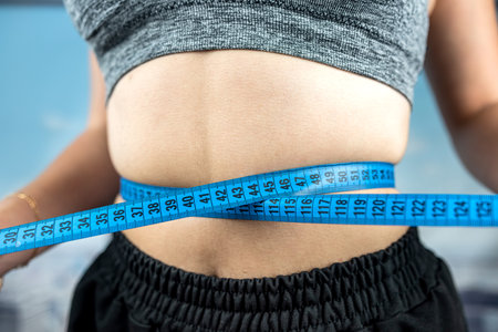 Young beautiful woman measuring perfect slim figure with tape measure in gym with panoramic windows. diets Healthy Lifestyle. fitnessの写真素材