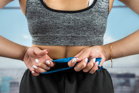 Young beautiful woman measuring perfect slim figure with tape measure in gym with panoramic windows. diets Healthy Lifestyle. fitnessの写真素材