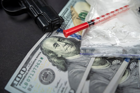 Heroin drug scattered next to syringes with money dollars and weapons isolated on dark background. concept of crime and drug addiction. the fight against drugs. violation of the lawの写真素材