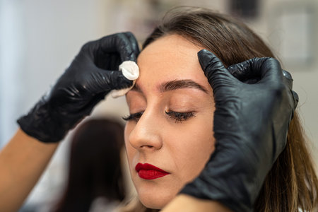 beautiful young client is wiping her eyebrows after painting them. the master wipes the paint.の写真素材