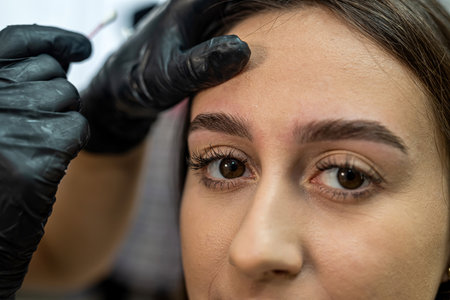 young beautiful girl client in the salon where the master corrects eyebrows. The concept of laminating and dyeing eyebrowsの写真素材