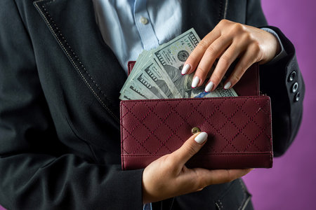 Close-up of a woman's hands putting a hundred dollar bill into her purse. Focus on the Purse. money. dollars in walletの写真素材
