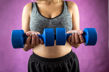 Portrait of cropped young attractive fitness woman holding dumbbells in studio on monochrome background. Sportswear of a girl in training with a strong beautiful slim body shape. lifestyle.の写真素材
