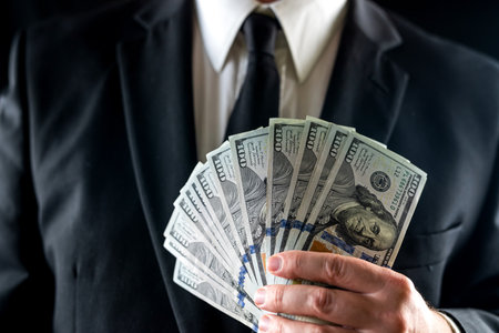 businessman in a shirt and jacket counts hundred dollar bills in front of his chest. Concept of money and trade. Up closeの写真素材