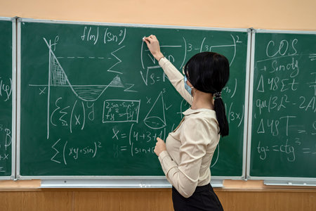 Caucasian young female teacher wearing face mask learn mathematics in classroom. School study during coronavirus epidemicの写真素材