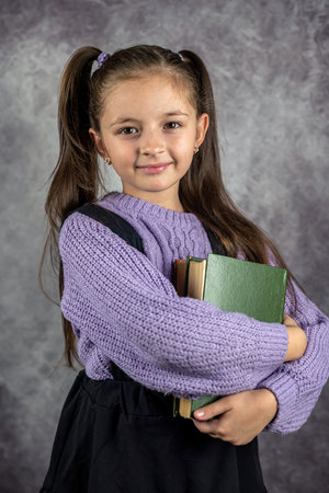 cute little girl is holding a book or books on a plain wall background in a studio. The concept of a girl with books. isolated teachingの写真素材
