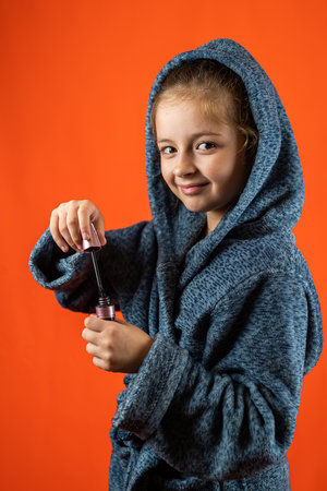 Close-up portrait of a little girl with a makeup brush and mascara near her face. isolated on orange background. make-up for childrenの写真素材