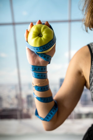 The coach holds a green apple in his hands and a measuring tape for measuring the body is wound on his hand. healthy lifestyle conceptの写真素材