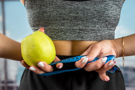 The coach holds a green apple in his hands and a measuring tape for measuring the body is wound on his hand. healthy lifestyle conceptの写真素材