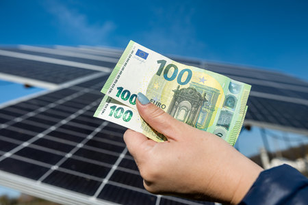 beautiful young well-groomed hands hold a large sum of euros near installed solar panels. Concept of green electricity. we care about the planetの写真素材