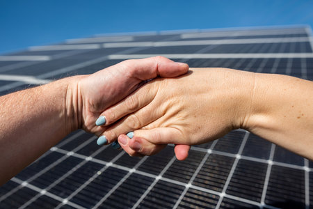 Handshake in front of solar energy photovoltaic panels outdoors. concept of agreement before installing solar panelsの写真素材
