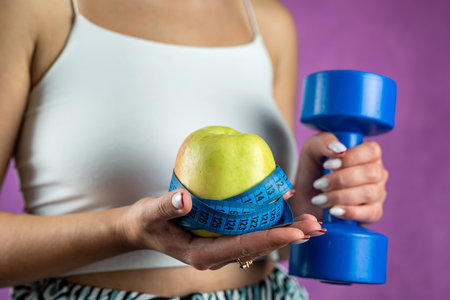 Slim unrecognizable woman with tape measure holding blue dumbbells and apple. Concept of weight loss and healthy lifestyle.の写真素材