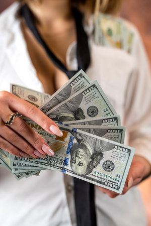 photo of a faceless woman holding dollar bills in her hands and counting them isolated on a smoky...
