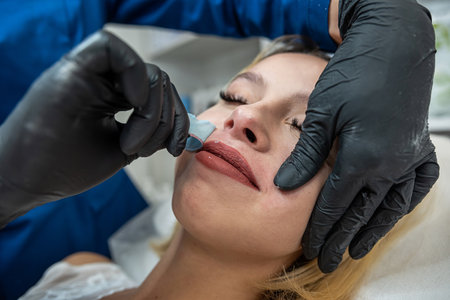 Beautician is removing hair mustache on lip female client face with wax hot sugar on spa salon. Epilation conceptの写真素材