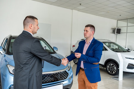 serious man buys an expensive car from a representative of a car dealership and shakes his hand as a sign of agreement. buying and selling cars. car dealershipの写真素材