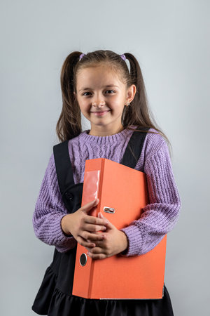 smiling beautiful cute little girl holding thick books in her hands isolated on plain background. the concept of a school girl. books in the hands of a childの写真素材