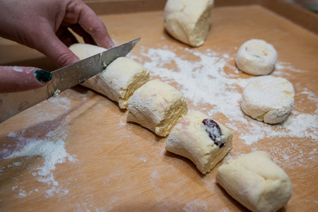 closeup of female hands in flour with a knife cut dough sausage in small pieces on a wooden board. Ukraine tasty traditional foodの写真素材