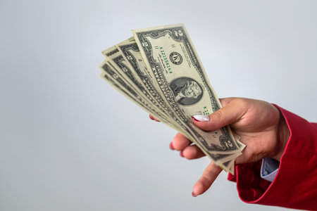 lady holding cash fans of dollars in hands in white shirt and red jacket isolated on solid color...