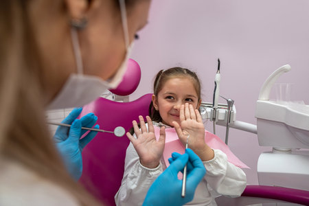 cute little girl is sitting on the dental chair and does not want to treat her teeth by showing appropriate gestures. concept of fear of dentists. healthy oral cavityの写真素材
