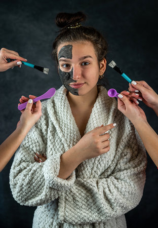 Young beautiful woman applies a restorative black mask with brush to her face isolated on dark. health care lifestyleの写真素材