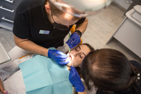 Treatment of a carious tooth in the office of a dental clinic. The dentist performs teeth cleaning and root canal treatment and filling. the assistant sterilizes the mouth with a saliva aspirator.の写真素材