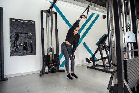 Portrait of a beautiful fitness lady working out in the gym doing exercises that pump back muscles....