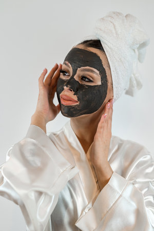 pretty sexy woman applying clay black mask on white background. Skin care, spa treatments for perfect skinの写真素材