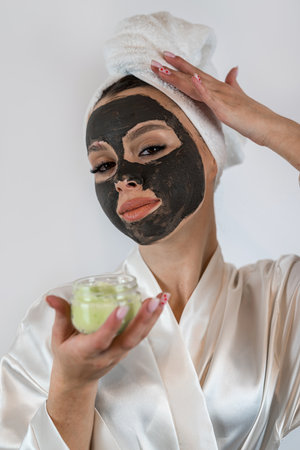 pretty sexy woman applying clay black mask on white background. Skin care, spa treatments for perfect skinの写真素材