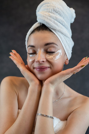 Girl wearing white towel use eye patches for puffiness, wrinkles isolated on black. Black collagen patches for skin careの写真素材