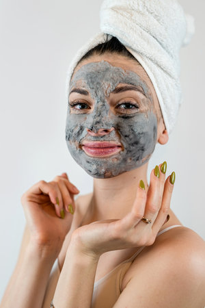 Young womanin white towel applying mud black mask on her face isolated on white, spa treatments at home. Perfect skin conceptの写真素材