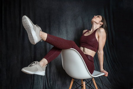 Athletic brunette young woman wear clort bra sitting on chair at studio shoot. sport lifestyle