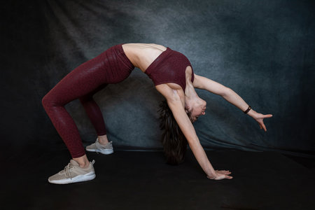 Caucasian slim girl in red sportswear make morning stretching exercises at blackstudio background....