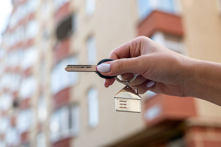 Men's hands holding a key with a keychain in the shape of a house on the background of a cool house. The interior of a modern bright lobby. Mortgage concept. real estate. moving or renting real estateの写真素材