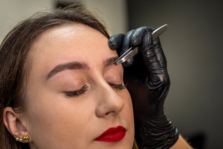 Close-up of a young woman during an eyebrow correction procedure in a beauty salon. tweezers. eyebrow epilationの写真素材